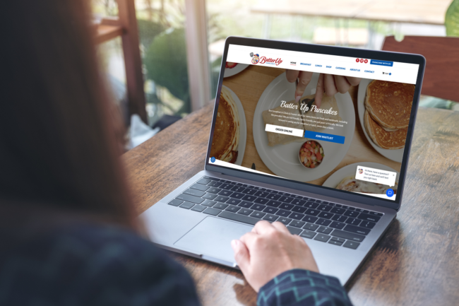 woman is looking at the batter up pancakes website from the convenience of her laptop at a cafe