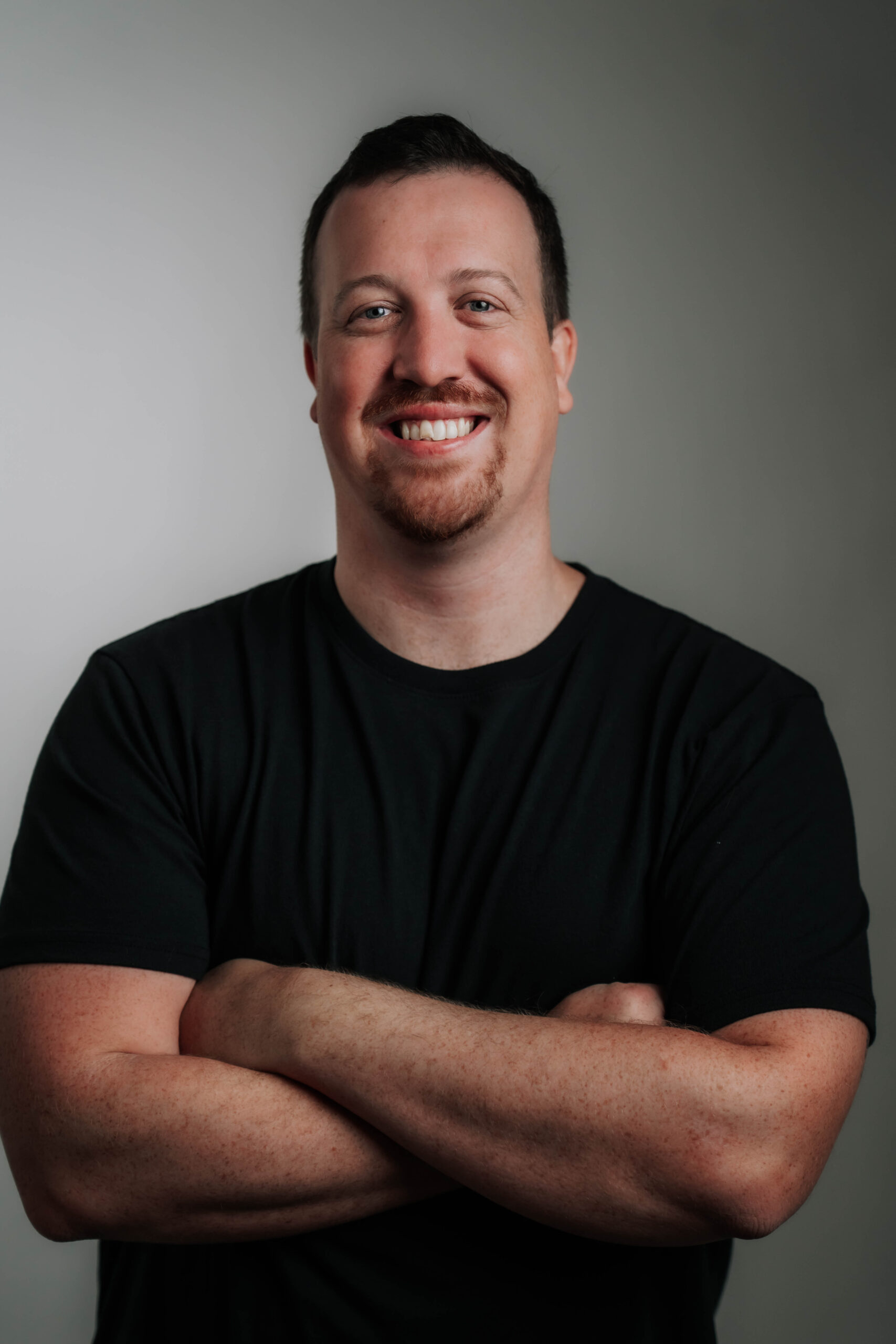 An engaging professional headshot of Dyllon Ryan, Chief Marketing Officer for Advine Agency. Dyllon's enthusiastic smile and confident pose in a black t-shirt highlight his dynamic approach to innovative marketing and brand strategy.