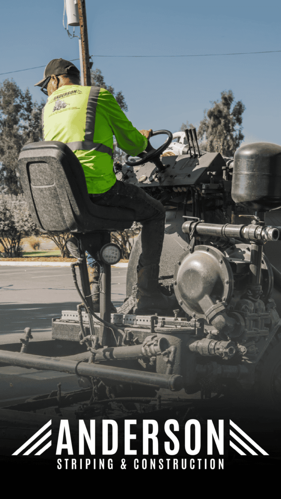 Anderson Striping Construction Advine's action photo for Anderson Striping & Construction features a worker in a bright safety vest operating a heavy-duty striping machine outdoors under a clear sky, illustrating the company's construction services.