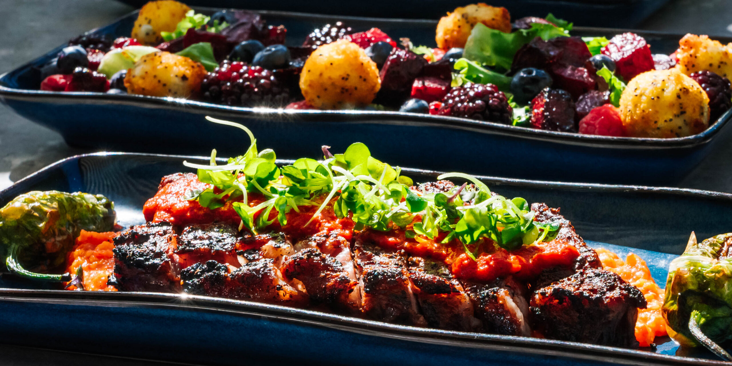 Group Food-1 "Three blue platters, expertly photographed by Advine's Photography Services in Fresno California, display a gourmet meal in natural light. The foreground shows a sliced, sauced steak with microgreens and blistered peppers. The middle platter features a vibrant salad of beets, berries, and golden croquettes,