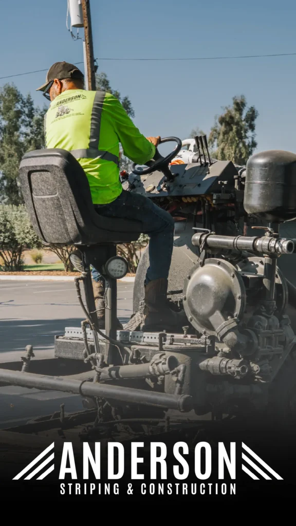 Advine's action photo for Anderson Striping & Construction features a worker in a bright safety vest operating a heavy-duty striping machine outdoors under a clear sky, illustrating the company's construction services.
